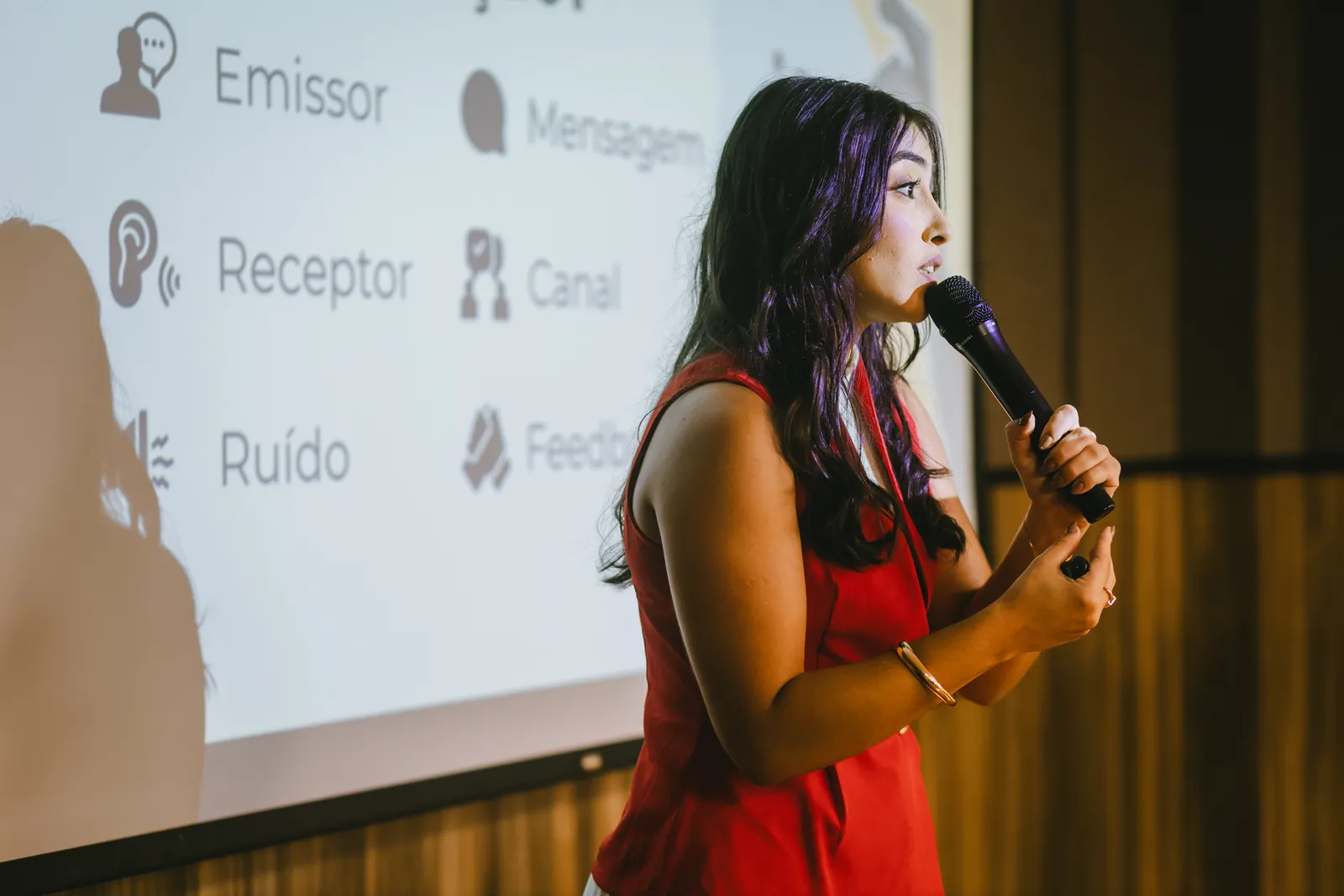 Ynnara palestrando com microfone diante de um slide sobre comunicação